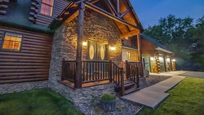 A log cabin with a stone foundation, a wooden porch, and a stone fireplace.