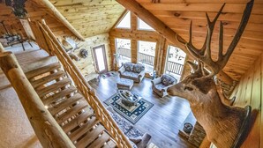 A wooden cabin with a staircase, a living area with a fireplace, and a mounted deer head.