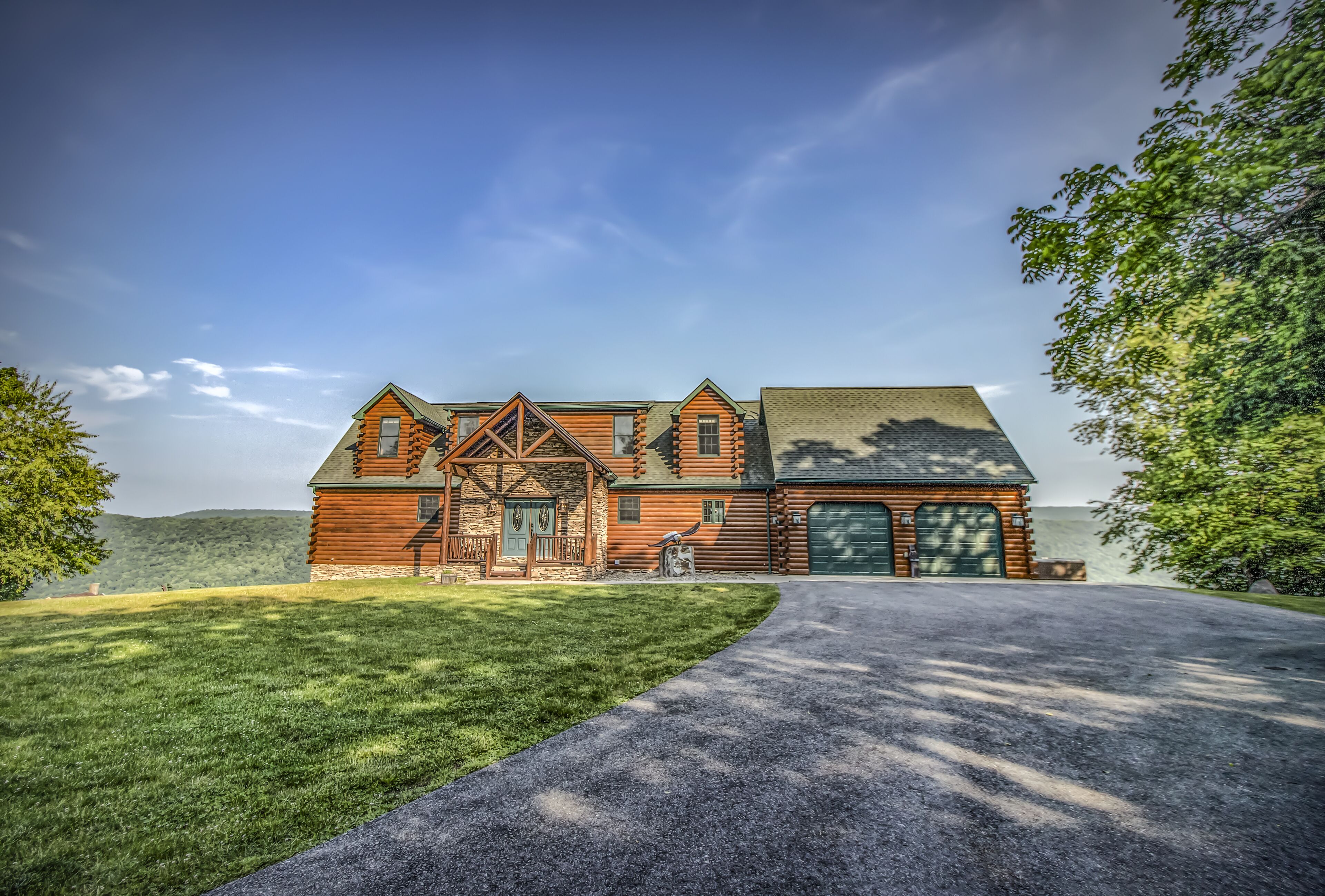 A large log cabin with a garage, surrounded by a well-maintained lawn and a driveway leading to the entrance.