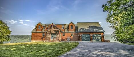 A large log cabin with a garage, surrounded by a well-maintained lawn and a driveway leading to the entrance.