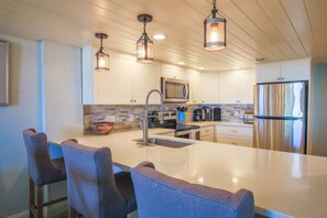 Une cuisine moderne dotée d’un îlot central, d’appareils électroménagers en acier inoxydable et de luminaires suspendus.