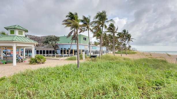 Un hotel fronte spiaggia con un padiglione a tetto verde, palme e una spiaggia sabbiosa.