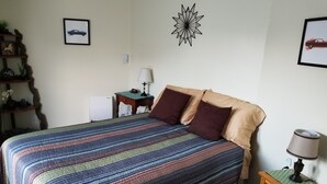 Una cama bien hecha con una colcha a rayas, una mesita de noche con lámpara y un reloj de pared.