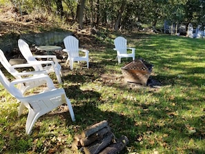 Outdoor seating with white plastic chairs and a metal fire pit.