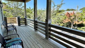 Eine Holzdiele mit Geländer, zwei Korbstühle und Blick auf Bäume sowie ein Haus im Hintergrund.