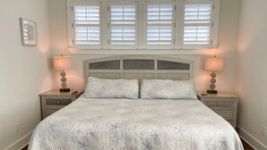 Ein Schlafzimmer mit einem Bett, zwei Nachttischen, einem Kopfteil und einem Fenster mit Jalousien.