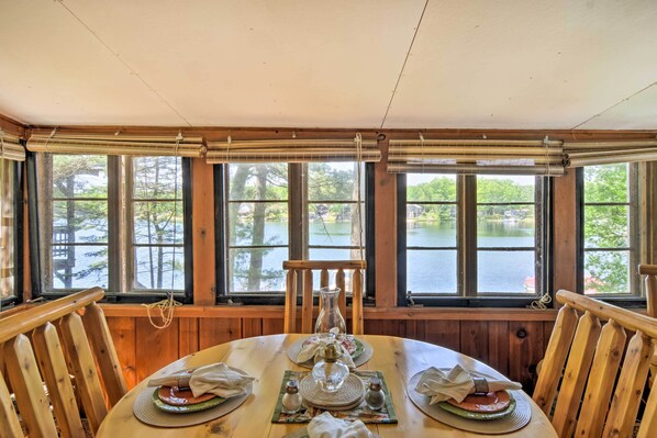 A wooden dining table set with plates, napkins, and a pitcher, overlooking a lake.