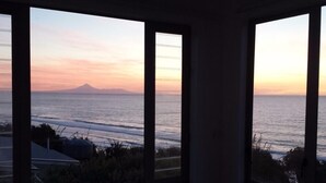 Blick aus einem Fenster auf einen Strand, im Hintergrund ein Berg.
