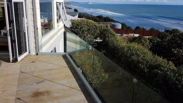 Ein modernes Haus mit einem Glasbalkon und Blick auf die Küste.