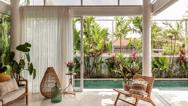 A spacious indoor area with a wooden ceiling, large windows, and a view of a swimming pool and greenery outside.