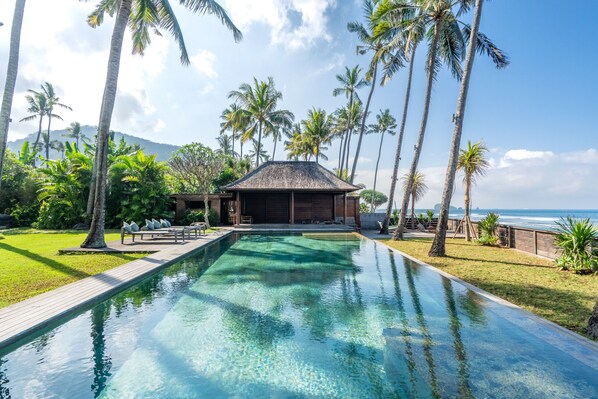 A swimming pool with a wooden deck, surrounded by palm trees and a view of the ocean.
