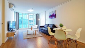 A modern living room with a sofa, a TV, a dining table with chairs, and a large window with curtains. - Premier Stays Melbourne (Southbank)