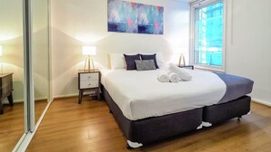 A bedroom with a large bed, a bedside table, a lamp, a mirror, and a window. - Premier Stays Melbourne (Southbank)