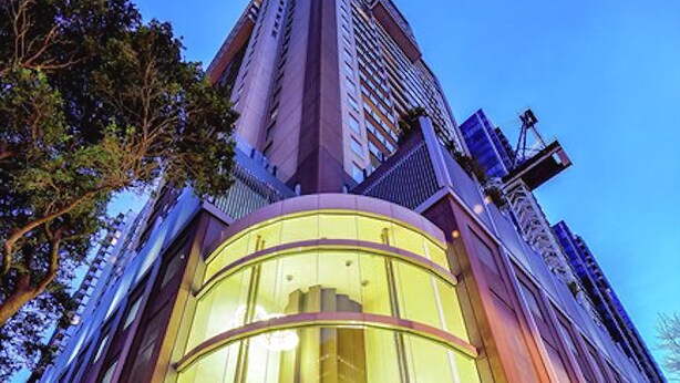 A modern building with a curved glass entrance and a tall structure in the background. - Premier Stays Melbourne (Southbank)