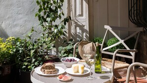A round metal table with a white chair, a bottle of wine, cheese, and bread on a tiled patio. - ★Romantic - Casa Bela ★ Apartment with private terrace and shared garden (Porto)