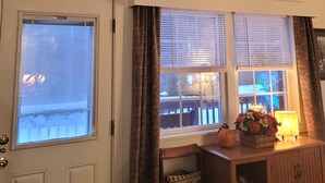 Een gezellige kamer met schuine plafonds, een deur met etsglas, een raam met zonwering, een klein tafeltje met een lamp en een welkomstbord.