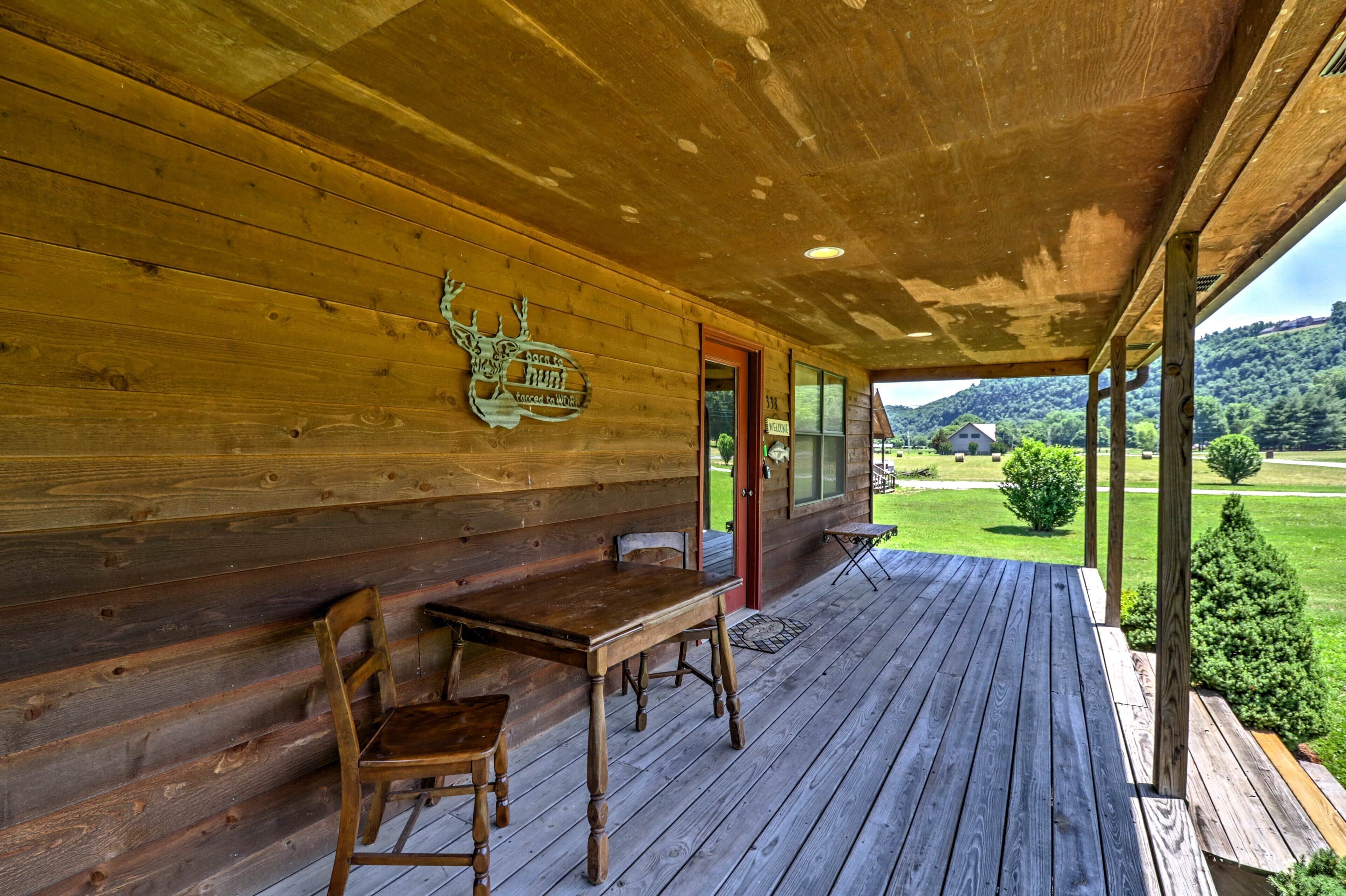 Une cabane en bois dotée d’un porche abrité, d’une table et d’une chaise en bois, et offrant une vue sur un paysage verdoyant.