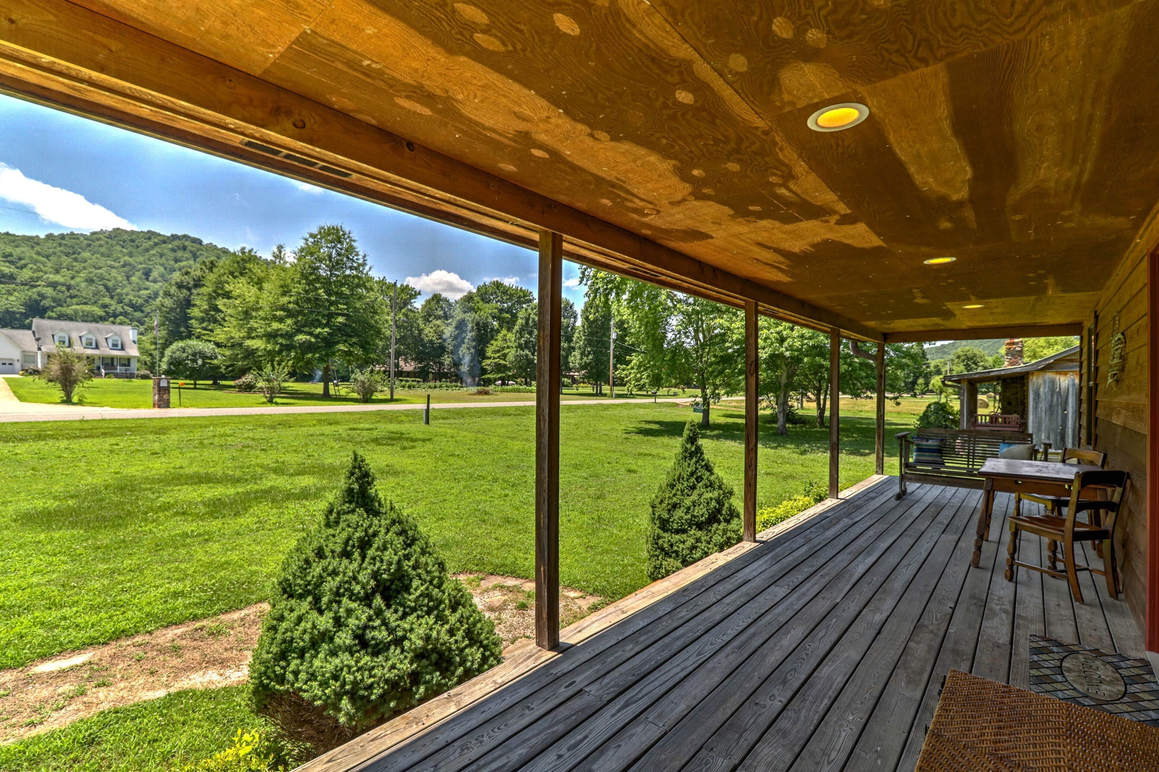 Une terrasse en bois avec une table et des chaises, donnant sur une pelouse bien entretenue et une maison située au loin.