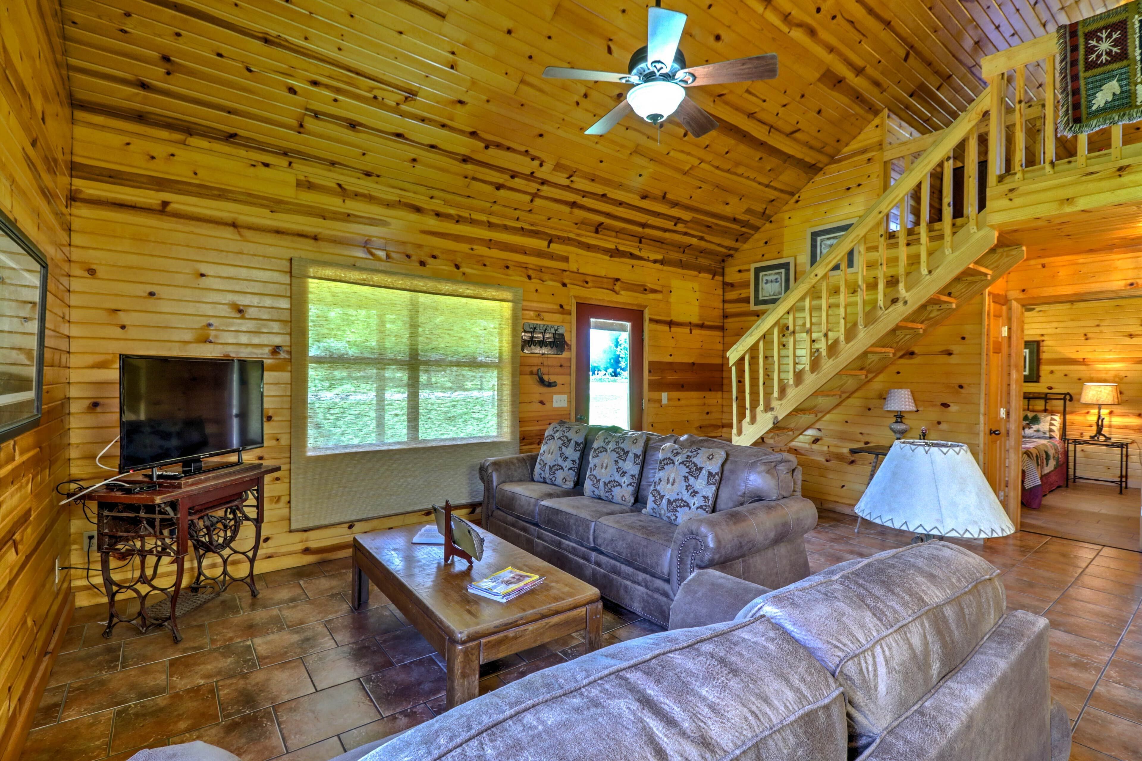 L'intérieur d'un chalet en bois, avec un canapé, un téléviseur et un escalier.