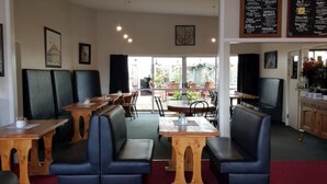 A restaurant with booths and tables, a menu board, and a view of the outside. - Hampden Hotel (Murchison)
