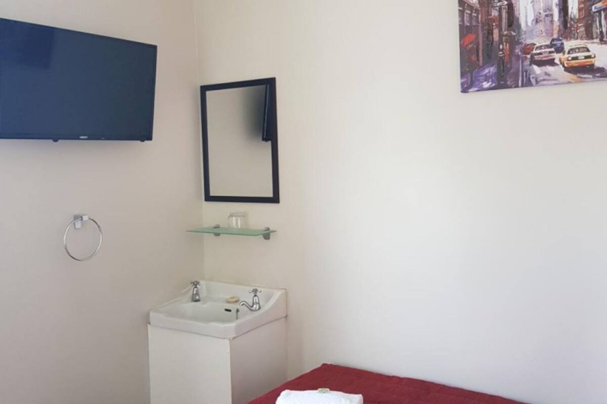 A small, clean room with a bed, a sink, a mirror, and a TV on the wall.