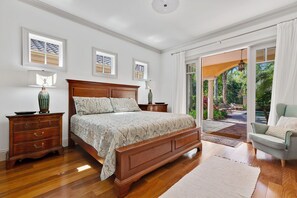 Une chambre à coucher avec un lit en bois, deux tables de chevet, une petite table et une vue sur le jardin, visible à travers une porte vitrée.