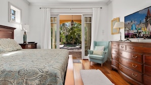 A bedroom with a large bed, a dresser, a chair, and a painting of a castle.