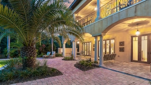A spacious outdoor patio with a brick pathway, palm trees, and outdoor seating.