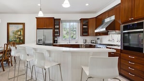 A modern kitchen with a large island, stainless steel appliances, wooden cabinets, and bar stools.