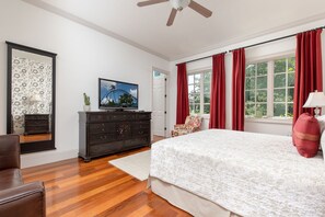 Un dormitorio con una cama grande, un aparador, un televisor y una ventana con cortinas rojas.