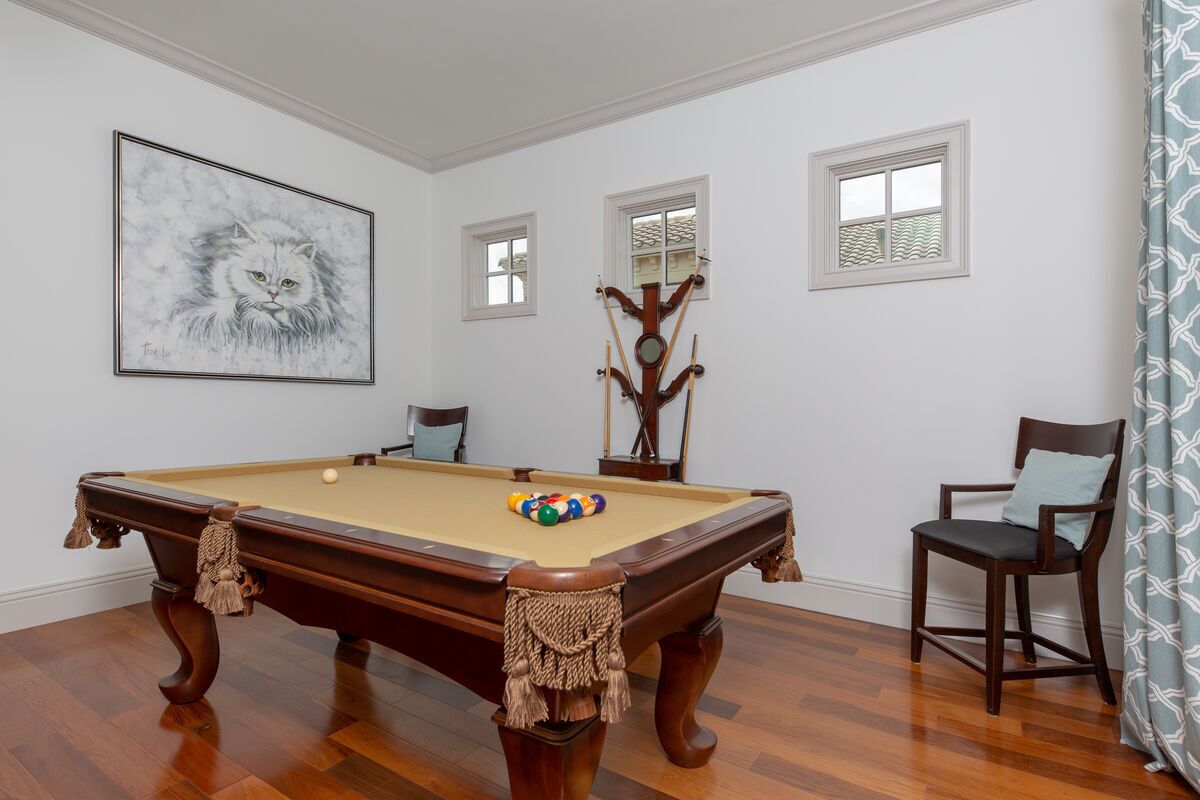 A pool table with a ball rack, a framed painting, and a wooden coat rack.