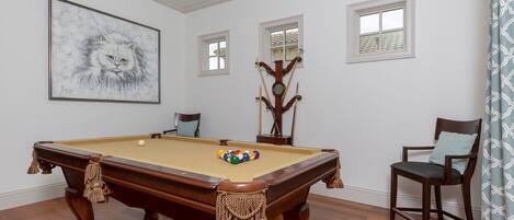 A pool table with a ball rack, a framed painting, and a wooden coat rack.