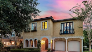 A two-story house with a brick driveway, arched windows, and a balcony.
