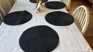 Una mesa de comedor con mantel blanco, individuales negros y un centro de mesa de mimbre.