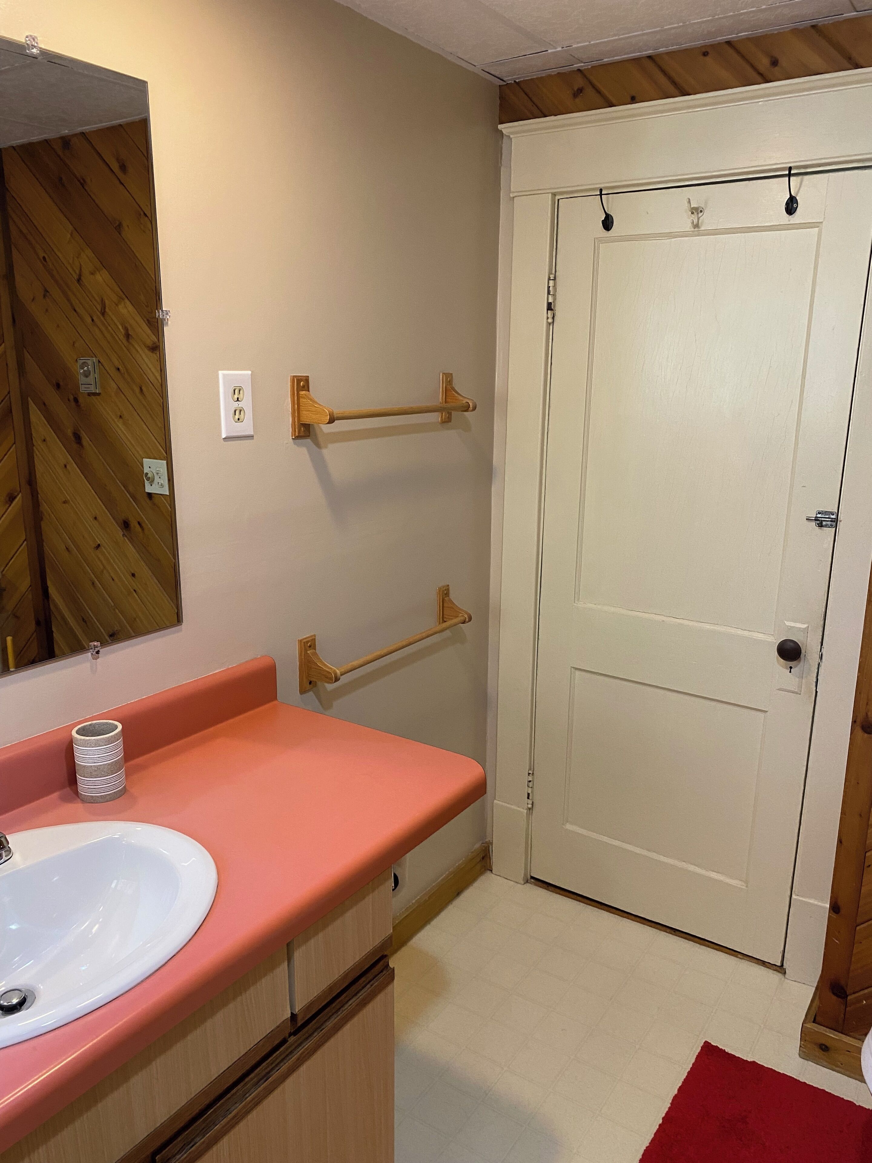Une salle de bain avec un meuble-lavabo en bois, un lavabo blanc et une porte au-dessus de laquelle se trouve un interrupteur.