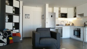 A modern kitchen with white cabinetry, a built-in microwave, and a dishwasher. There is a gray armchair in the living area, and a bookshelf with decorative items. - Friendly Beach House (4160 nettle baie beach club)