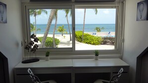 A room with a desk and two chairs, a window with a view of a beach and palm trees. - Friendly Beach House (4160 nettle baie beach club)