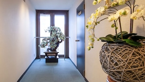 A hallway with a potted plant, a door with a number, and a framed picture on the wall. - Tabist Hotel Fuji (Daisen)
