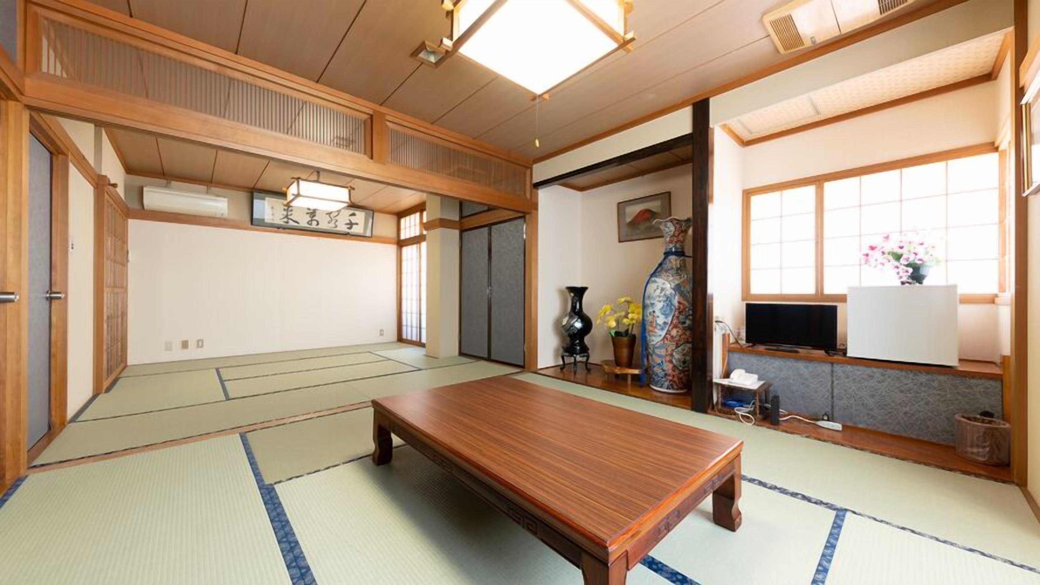 A traditional Japanese room with tatami flooring, a low wooden table, a TV, and a vase with flowers.