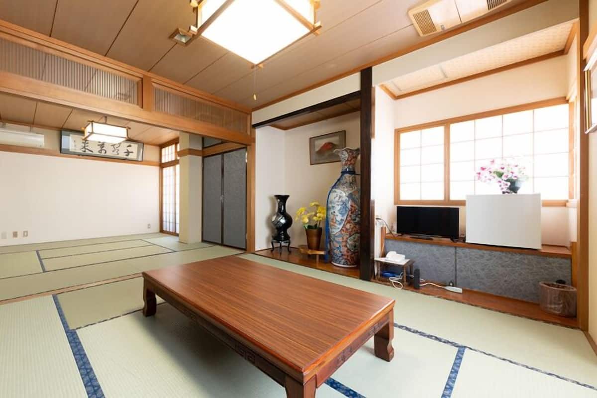 Une pièce de style japonais traditionnel, avec un sol recouvert de tatamis, une petite table en bois, un téléviseur et un vase rempli de fleurs.