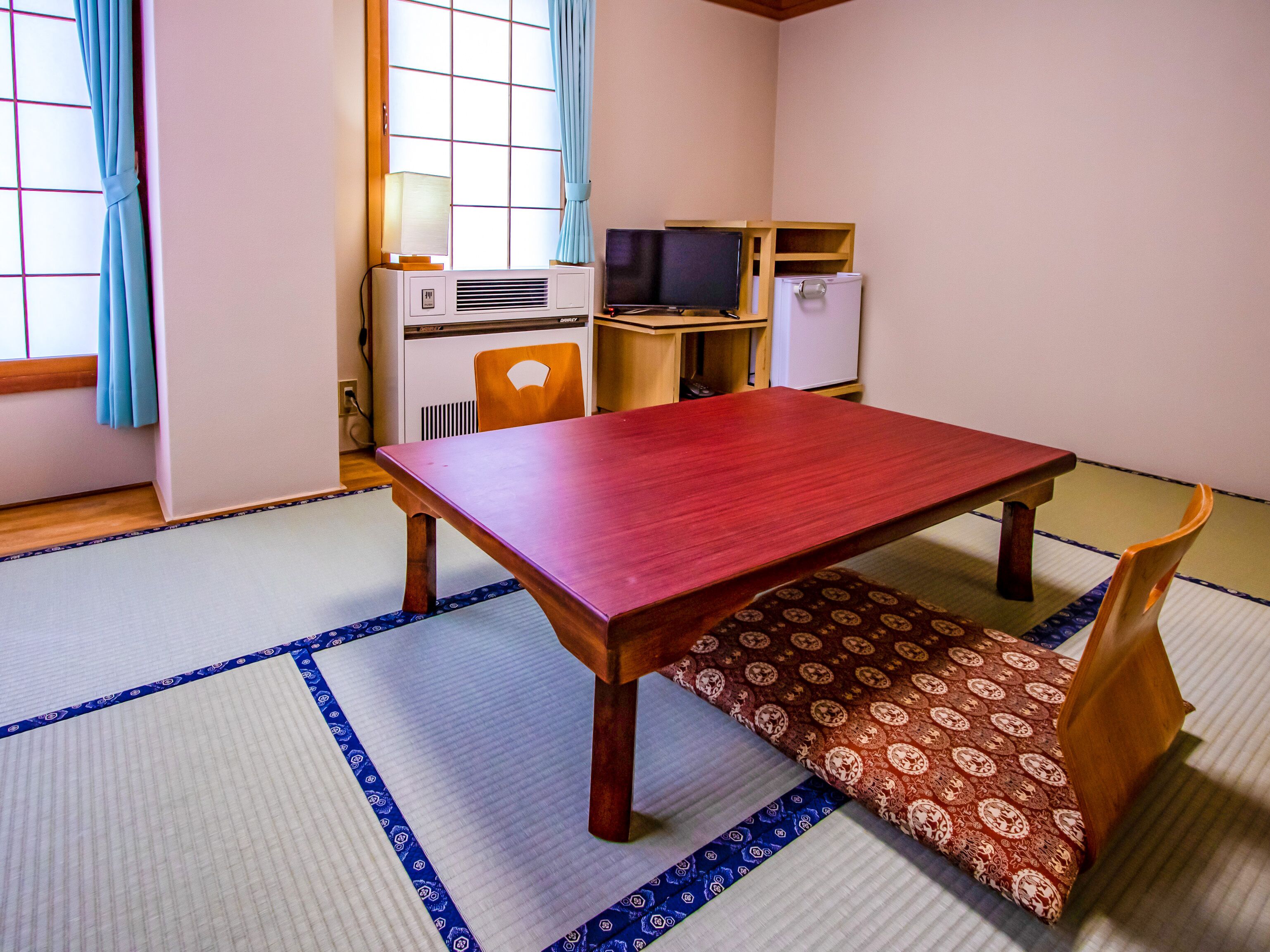 Una habitación japonesa tradicional con suelo de tatami, una mesa de madera, un televisor y un refrigerador.