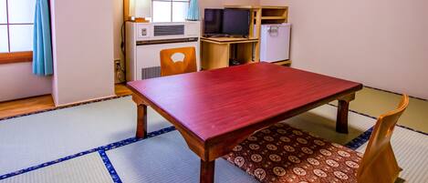 Una habitación japonesa tradicional con suelo de tatami, una mesa de madera, un televisor y un refrigerador.