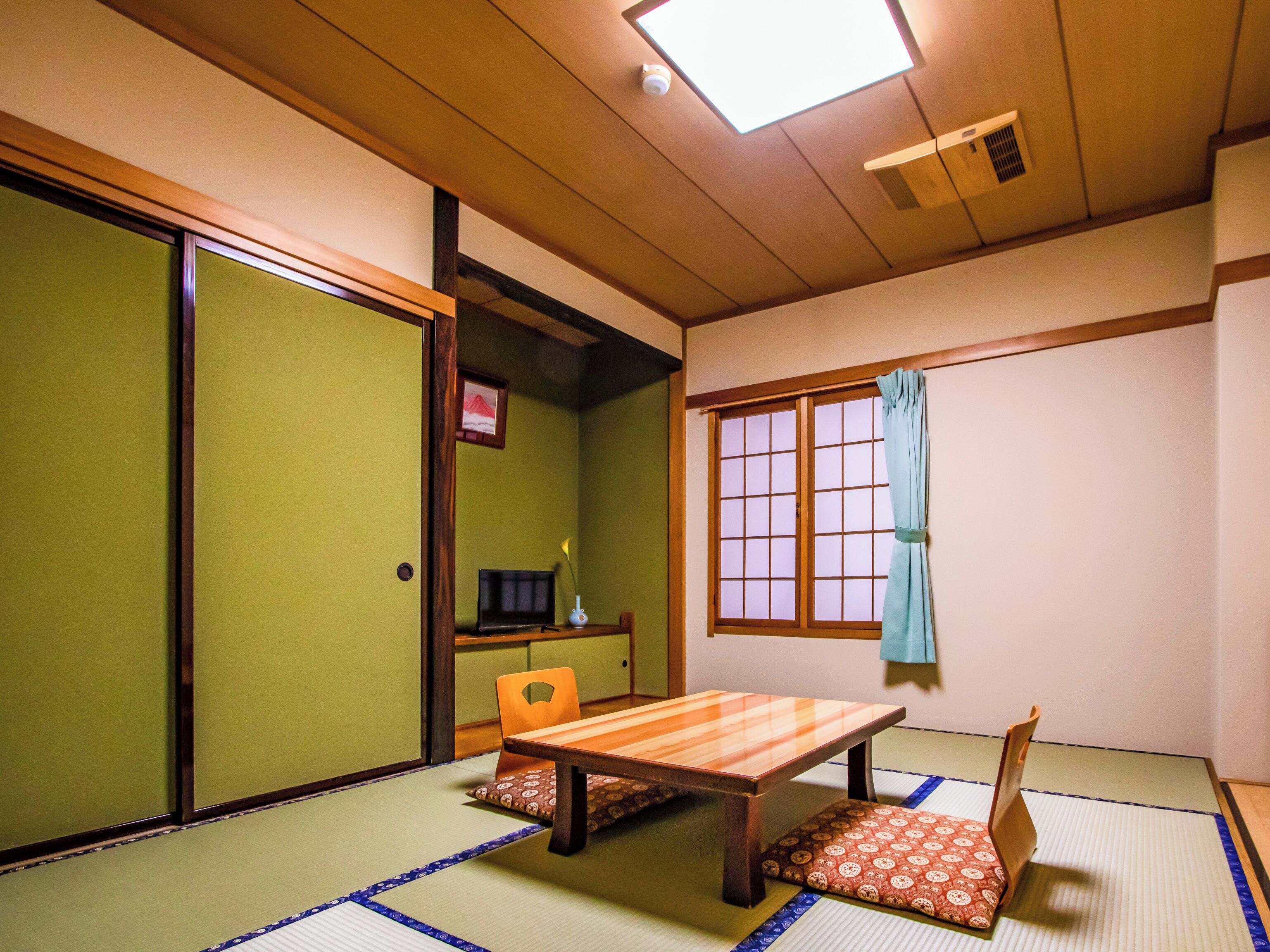 A traditional Japanese room with tatami flooring, a low table, a chair, a sliding door, and a window with a curtain.