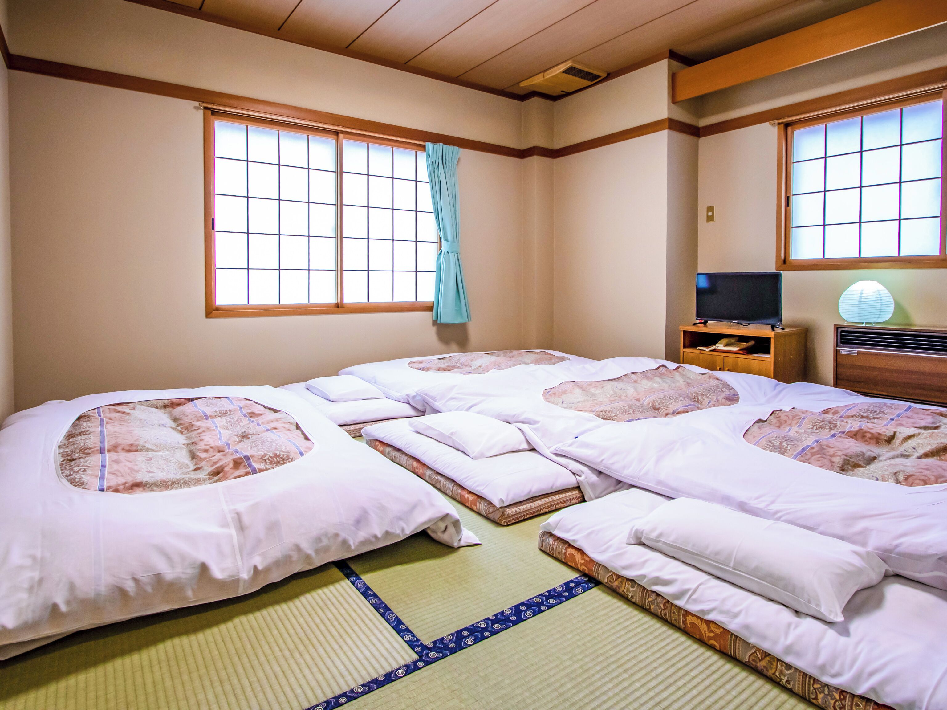 A traditional Japanese-style room with tatami mats, a futon bed, a television on a wooden cabinet, and a shoji screen.