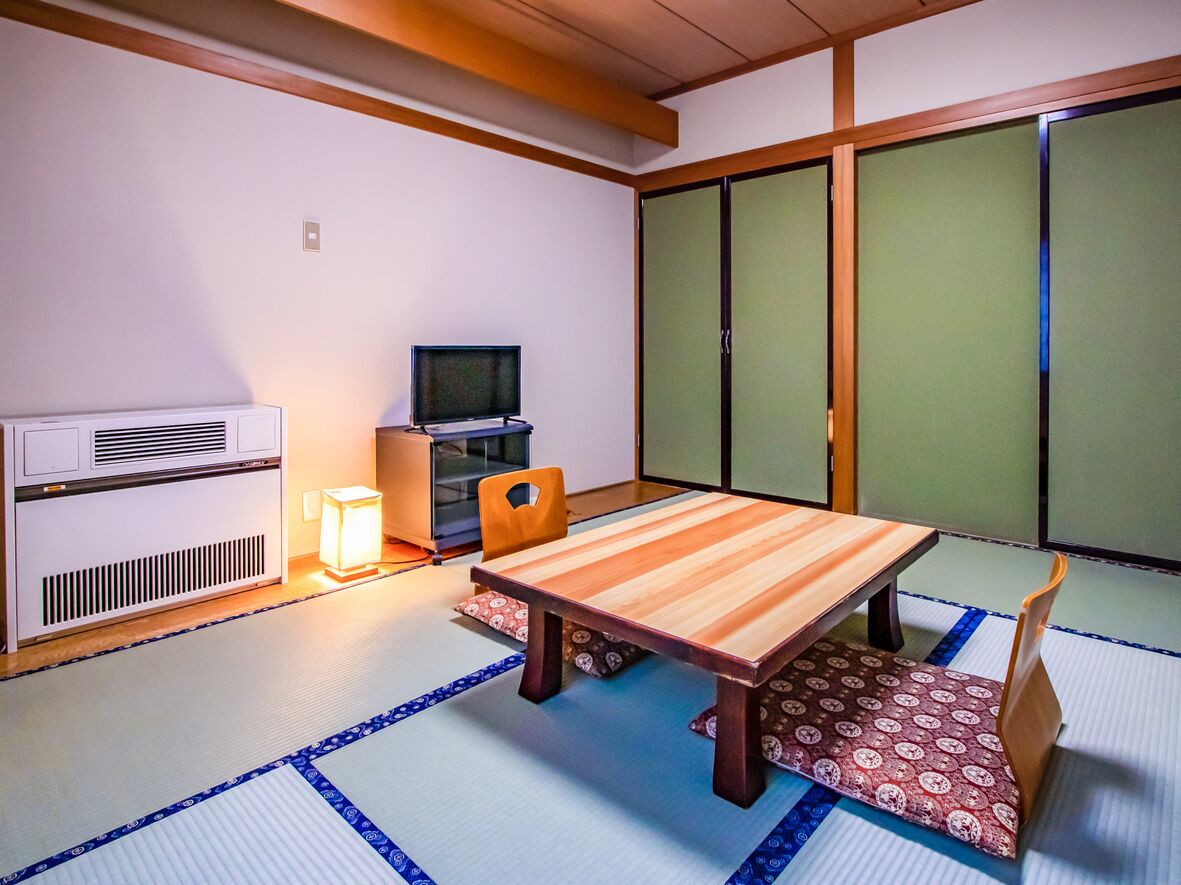 A traditional Japanese room with tatami flooring, a low table, a television, and sliding doors.