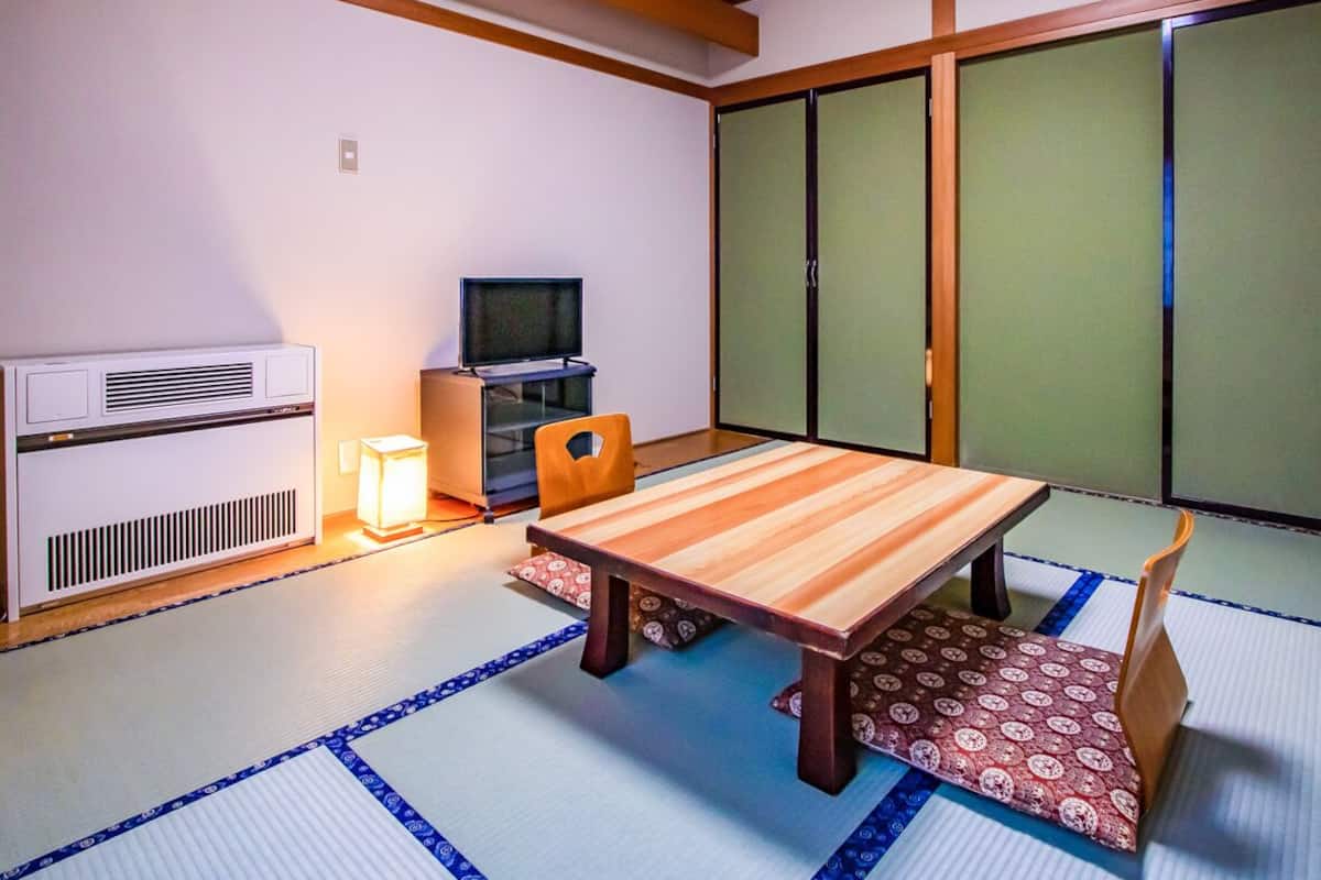 Une pièce de style japonais traditionnel, avec un sol recouvert de tatamis, une table basse, un téléviseur et des portes coulissantes.