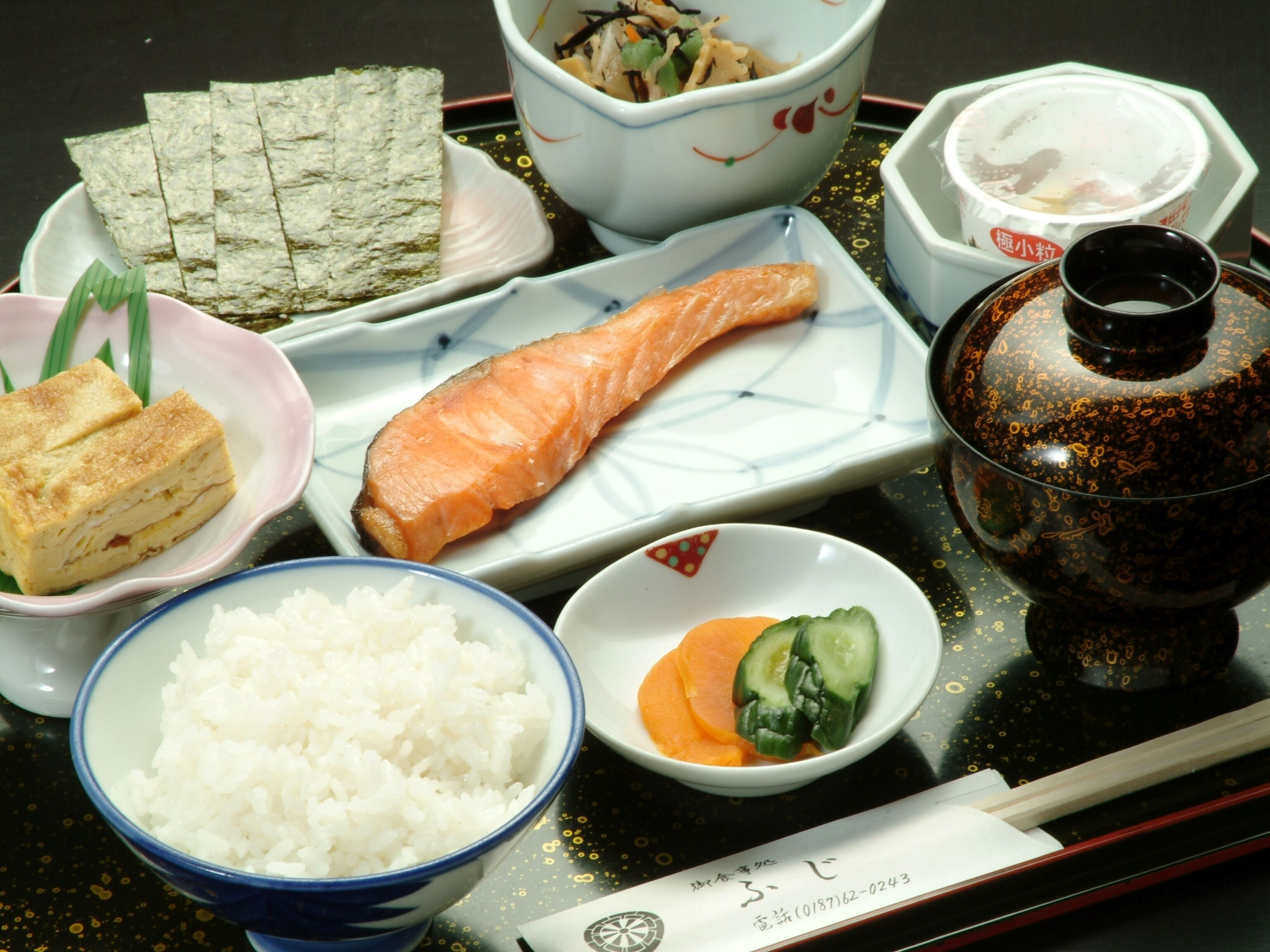 A traditional Japanese meal with rice, salmon, and pickled vegetables on a tray.