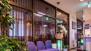 A reception area with a purple seating area, large windows with patterned curtains, and indoor plants. - Tabist Hotel Fuji (Daisen)