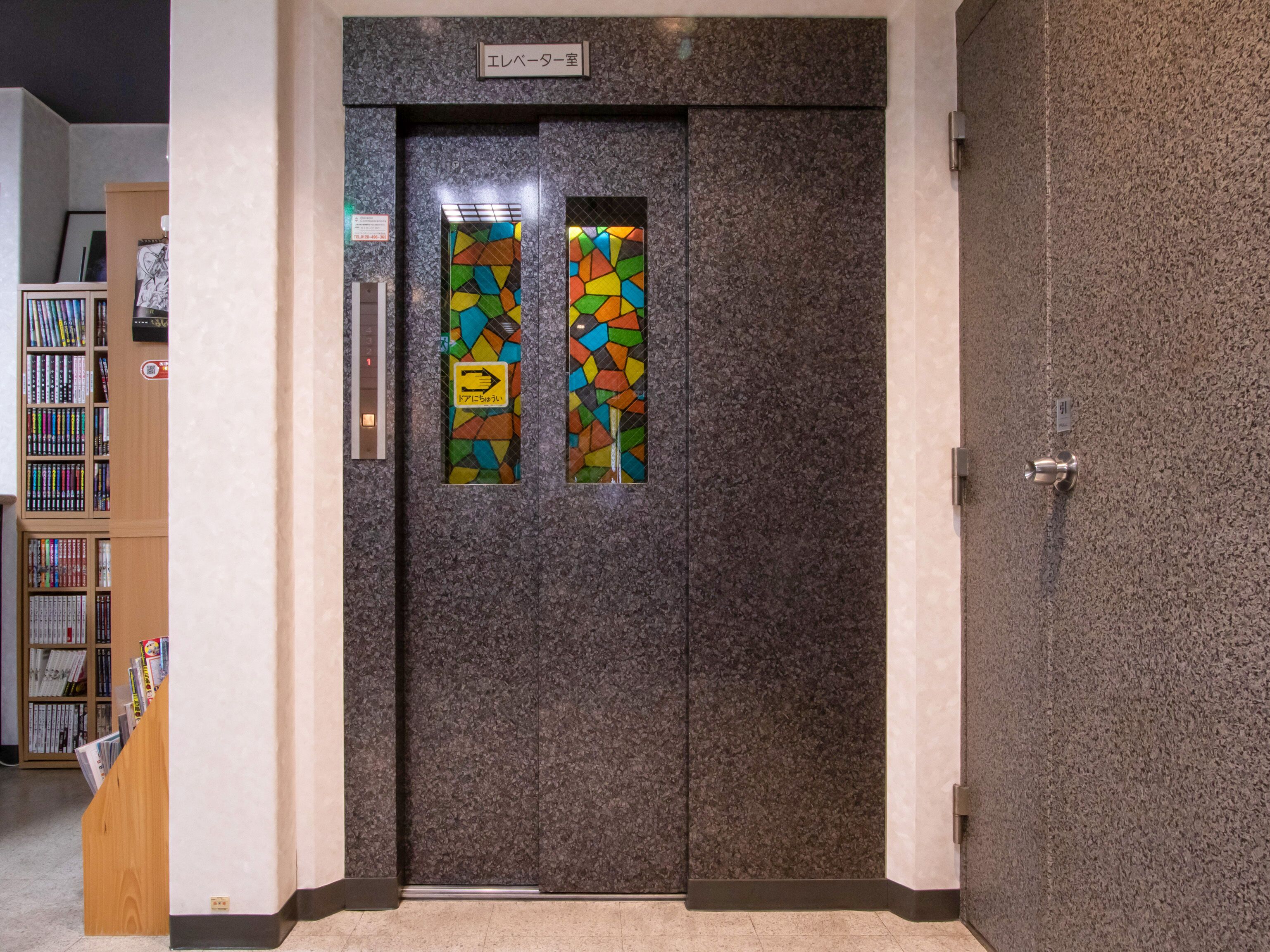 A hotel room entrance with a dark granite door, a small sign above the door, and a bookshelf with various items on the left.