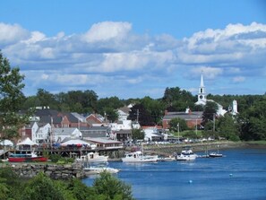 A coastal town with a prominent church steeple, a dock with boats, and buildings along the waterfront.